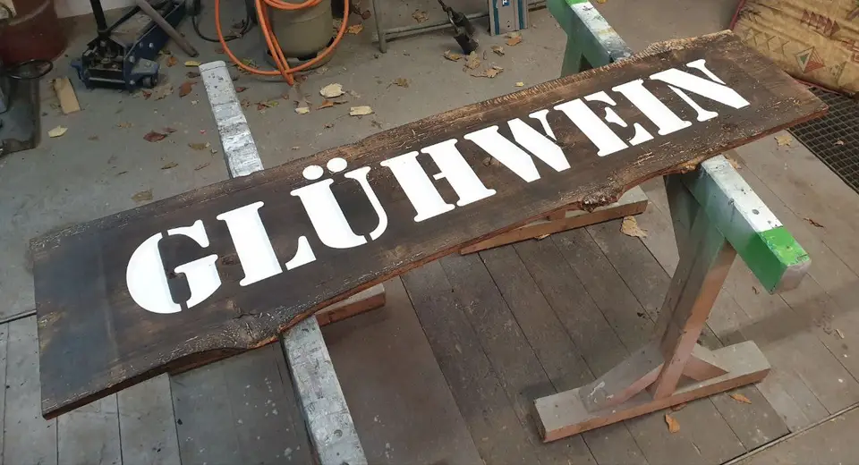 Ein langes rustikales Eichenschild mit dem gemalten Wort Glühwein