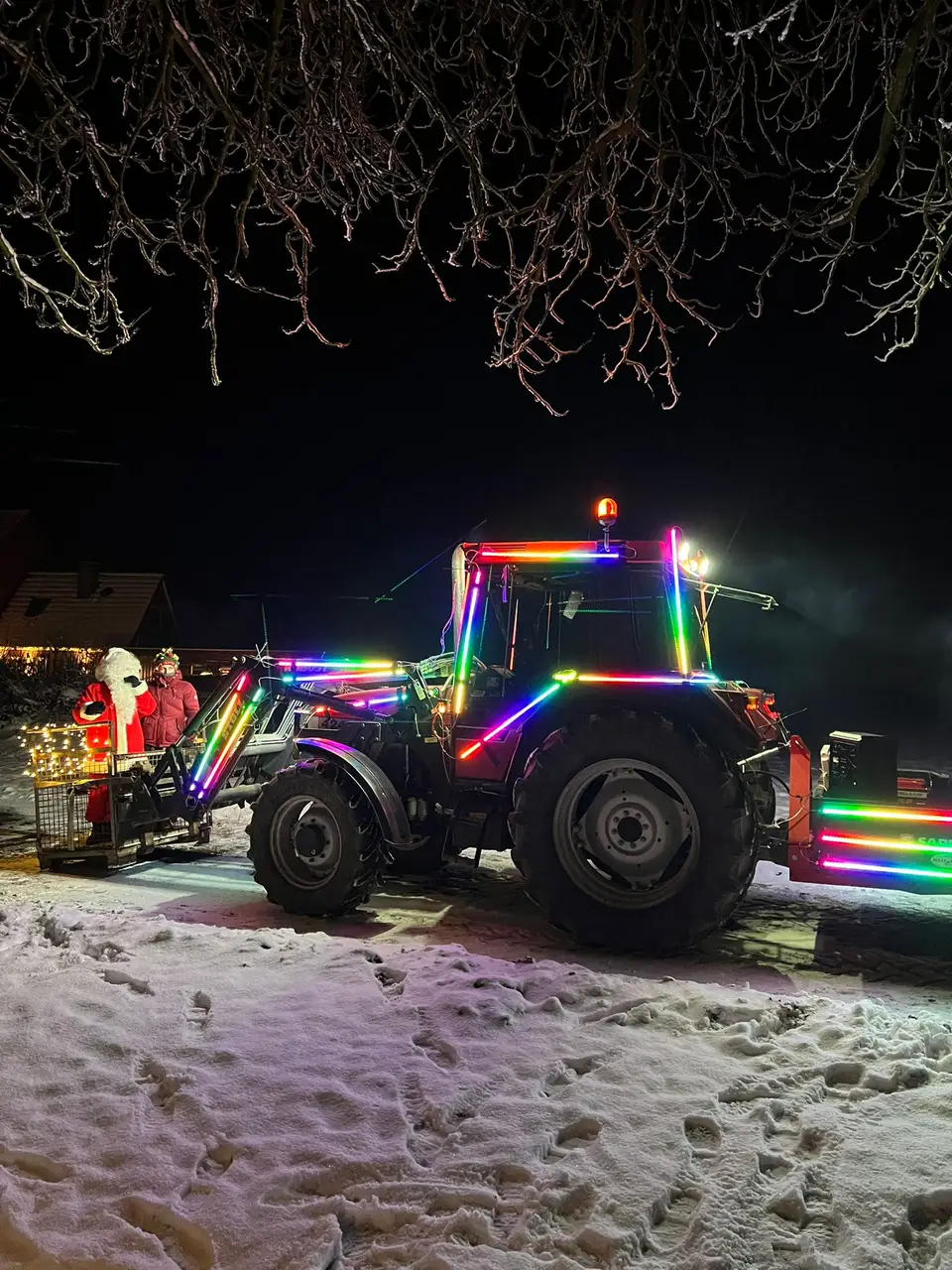 Ein mit bunten Lichtern geschmückter Traktor bei einer verschneiten Nachtveranstaltung